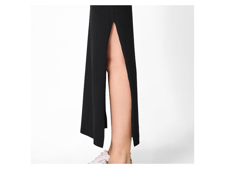 Zwarte lange rok met split, zichtbare benen en witte sportschoenen.