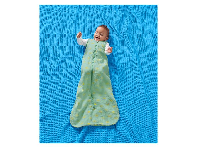 Blauwe deken met blije baby in groene slaapzak met zonnepatronen.
