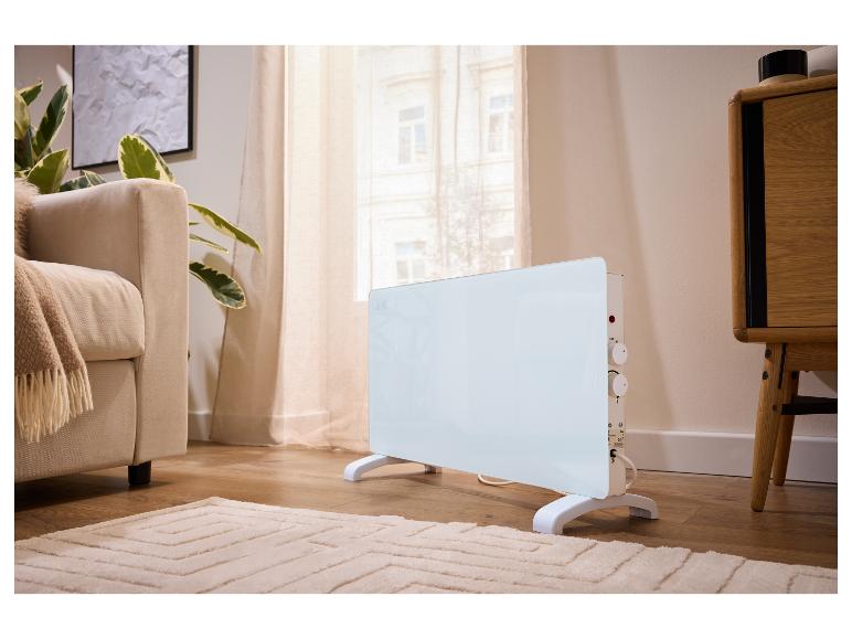 Witte vrijstaande verwarming in een moderne woonkamer met bank en planten.