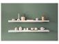 Twee witte zwevende planken aan een groene muur, versierd met diverse decoratieve items en keramiek.