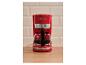 Rood koffiezetapparaat met een glazen kan gevuld met koffie, op een houten aanrecht.