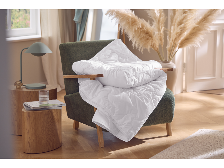 Witte deken op een fauteuil, houten bijzettafel met lamp en glas.