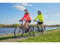 Een vrouw en een man die op elektrische fietsen rijden op een pad langs het water.