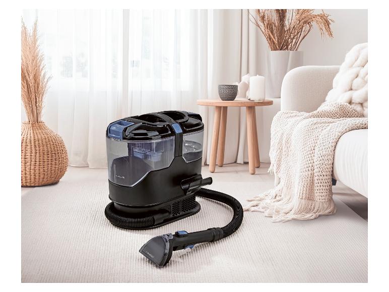 Tapijtreiniger met slang en mondstuk op een licht tapijt in een gezellige woonkamer.