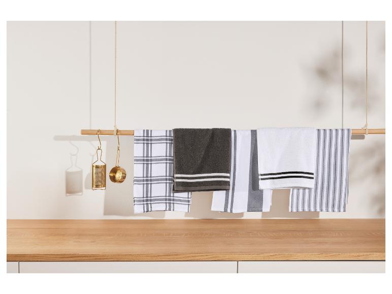 Diverse theedoeken hangend aan een houten stang, met gouden keukengerei.