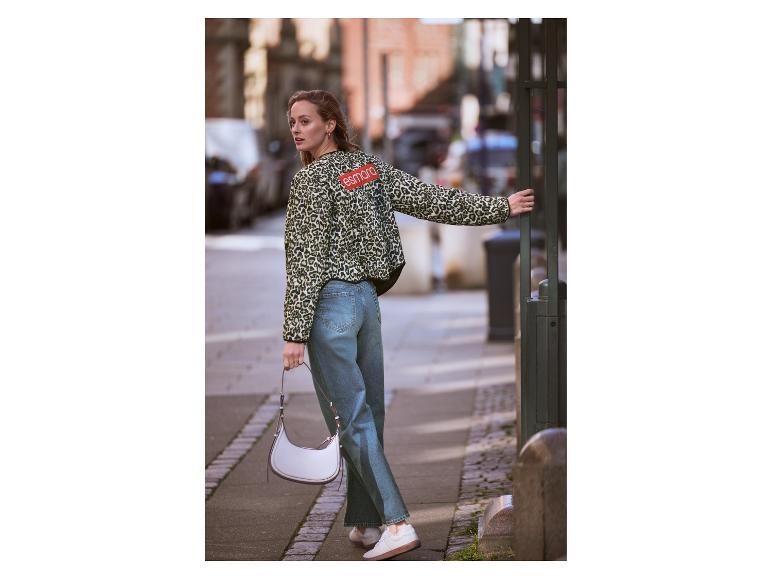 Vrouw in luipaardprint jasje en jeans met witte tas op een stadsstraat.