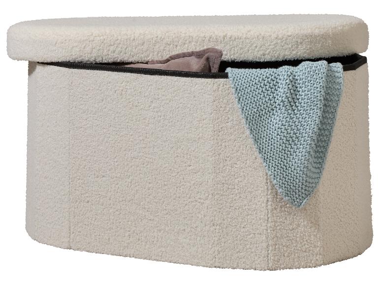 Crèmekleurige bouclé opbergpoef met een lichtblauwe gebreide deken en een bruine deken erin