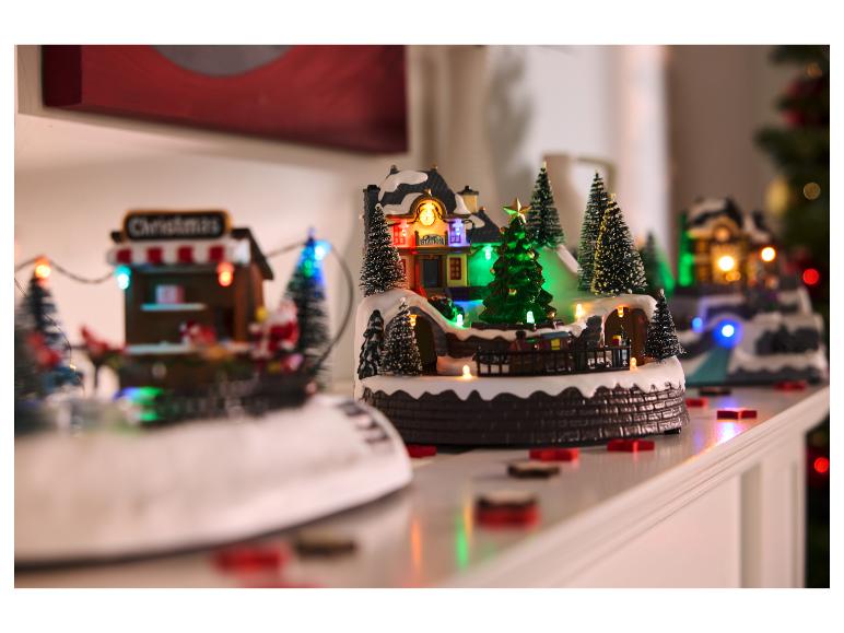 Een feestelijke kerstdorpdisplay met verlichte gebouwen, miniatuurbomen en een trein.