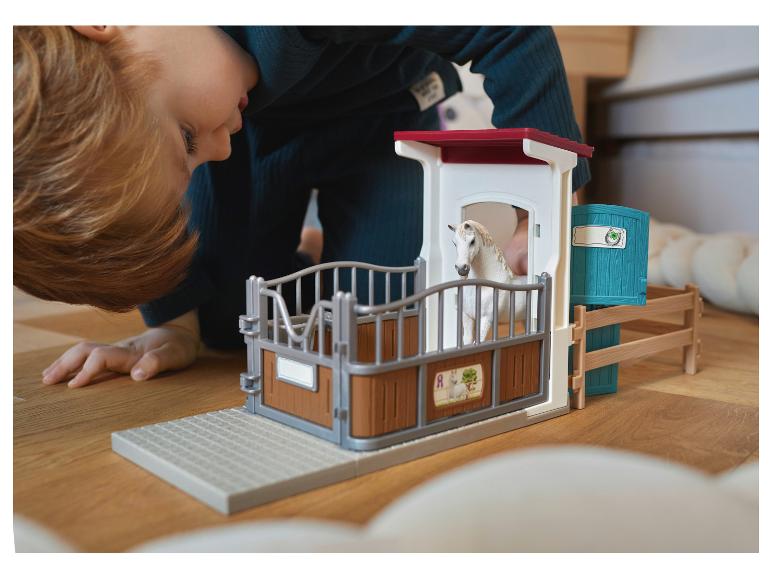 Kind speelt met speelgoedstal met wit paard op houten vloer.