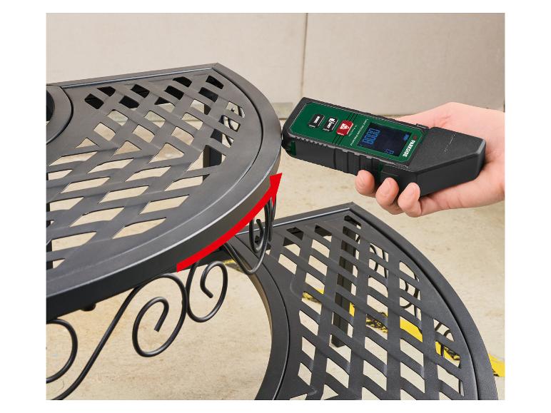 Een hand houdt een Parkside laserafstandsmeter tegen een zwart metalen rek.