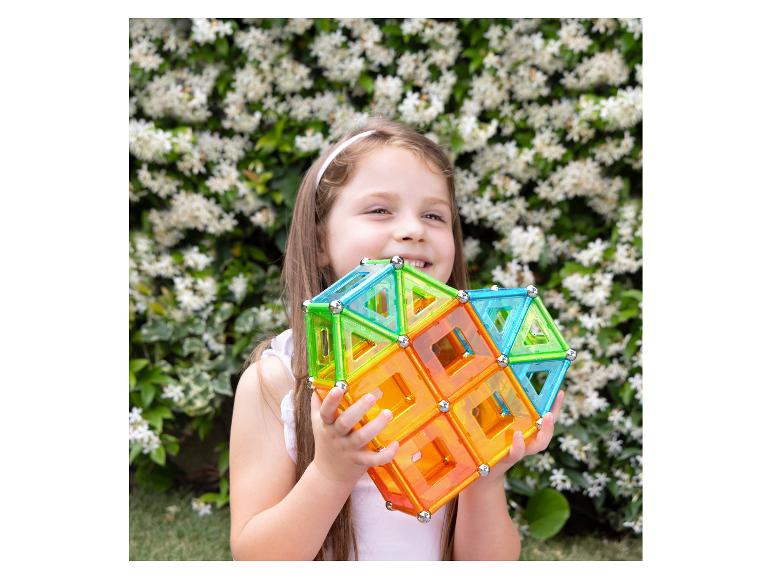 Meisje houdt kleurrijke magnetische bouwblokken vast voor een bloeiende struik.