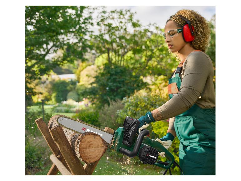 Vrouw in veiligheidsuitrusting zaagt hout met een Parkside kettingzaag in een tuin.