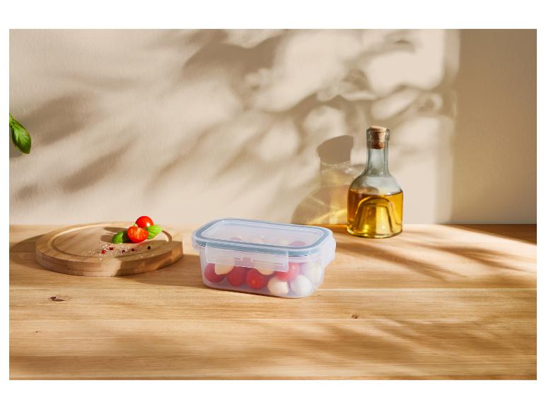 Container met cherrytomaten en mozzarella, olijfolie en kruiden op een tafel.