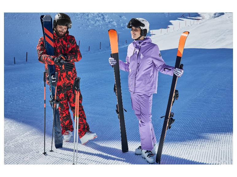 Twee skiërs in kleurrijke skikleding houden ski's en stokken vast op een geprepareerde piste.