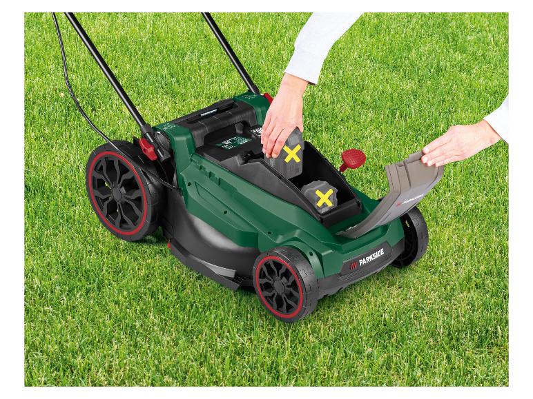 Een persoon plaatst batterijen in een groene grasmaaier op het gazon.