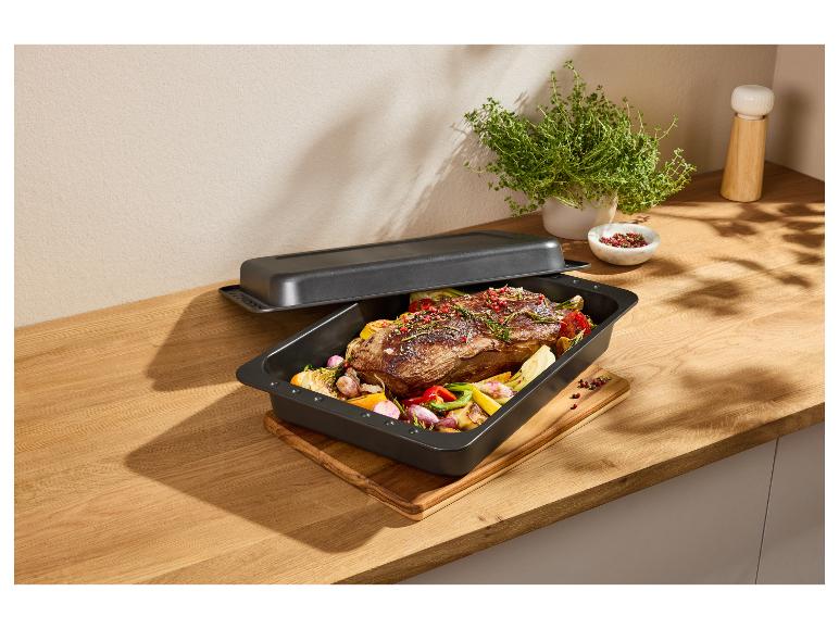 Braadslede met deksel en gebraden vlees met groenten op een houten aanrecht.