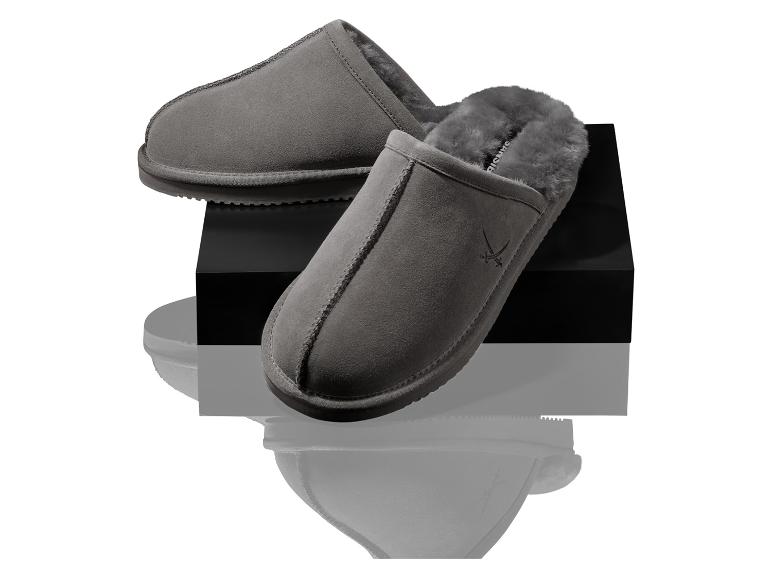 Een paar grijze suède pantoffels met bontvoering op een zwart voetstuk.