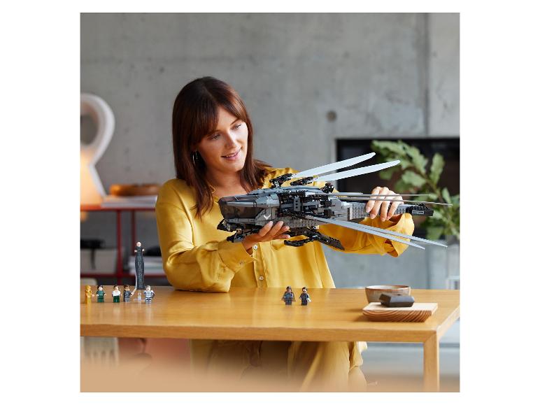 Een vrouw assembleert een groot ruimteschip van bouwstenen, met kleine figuren op tafel.