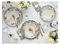 Elegant servies met bloemmotieven, gouden bestek en witte bloemen op een witte tafel.
