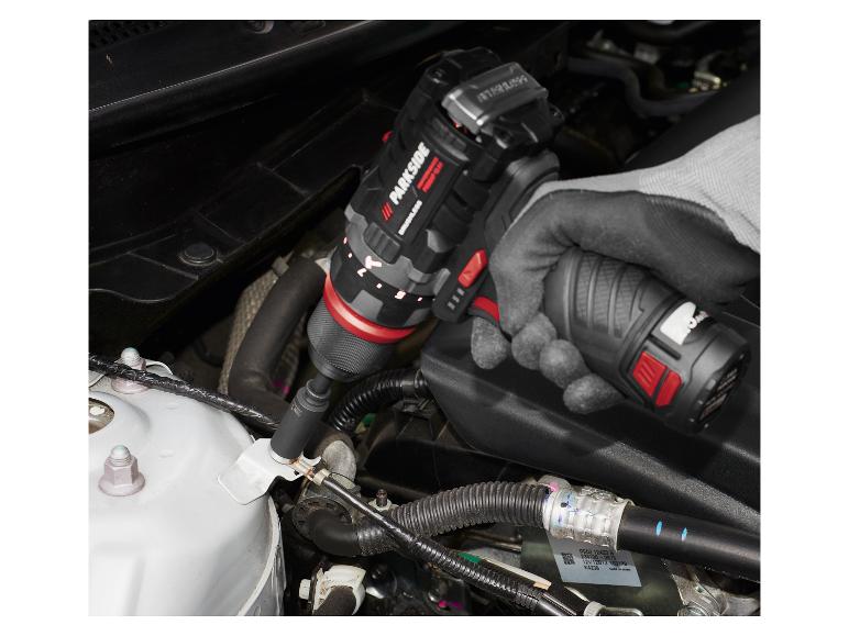 Een persoon gebruikt een accuboormachine om aan een automotor te werken.