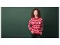 Een vrouw draagt een rode trui met kerstmotief voor een groene achtergrond.