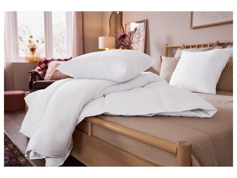 Wit dekbed en kussens op een licht houten bed in een gezellige slaapkamer.