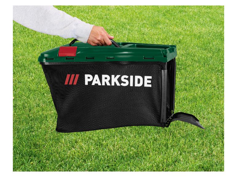 Hand die een zwarte Parkside grasopvangbak met donkergroen deksel vasthoudt op groen gras.