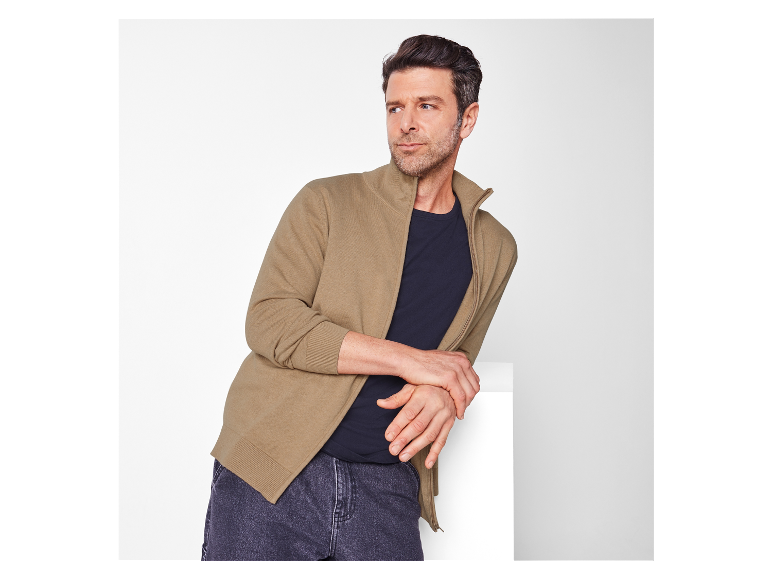 Een man poseert in een beige ritsvest.