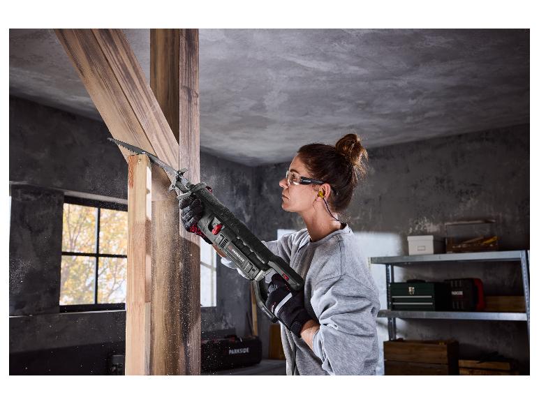 Vrouw gebruikt een Parkside reciprozaag om hout te zagen, met veiligheidsbril en oordopjes.