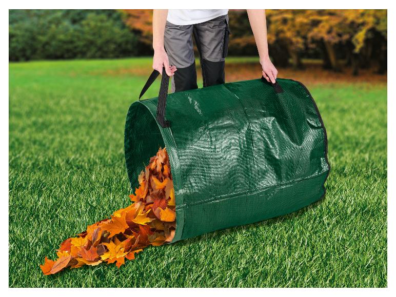 Persoon leegt een groene tuinafvalzak vol herfstbladeren op het gras.