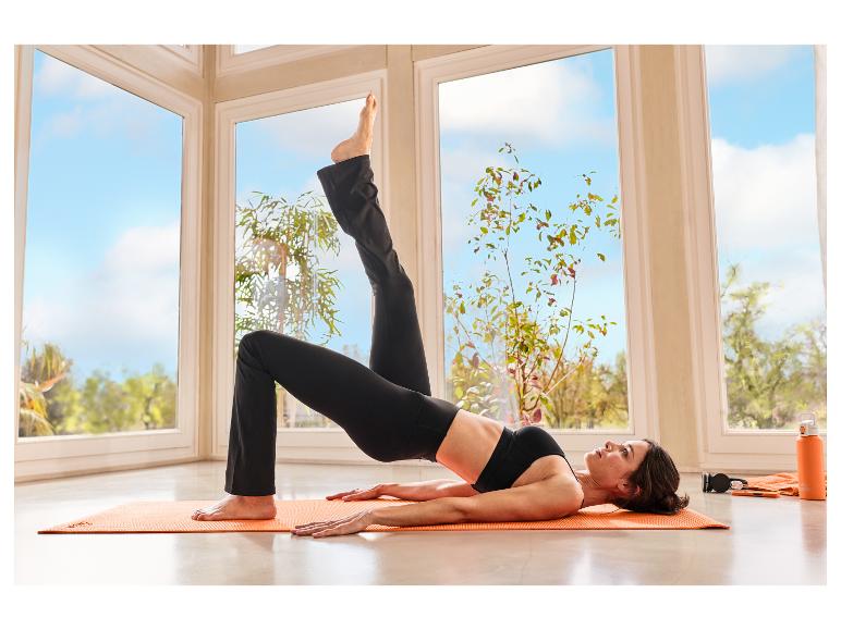 Vrouw in zwarte functionele sportlegging van CRIVIT doet yoga op een mat.