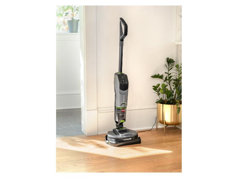 Bissell SpinWave + Vac vloerreiniger op houten vloer met planten op de achtergrond.