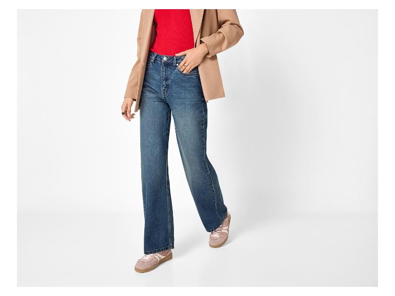 Vrouw in rode top, beige blazer, blauwe jeans en roze sneakers.