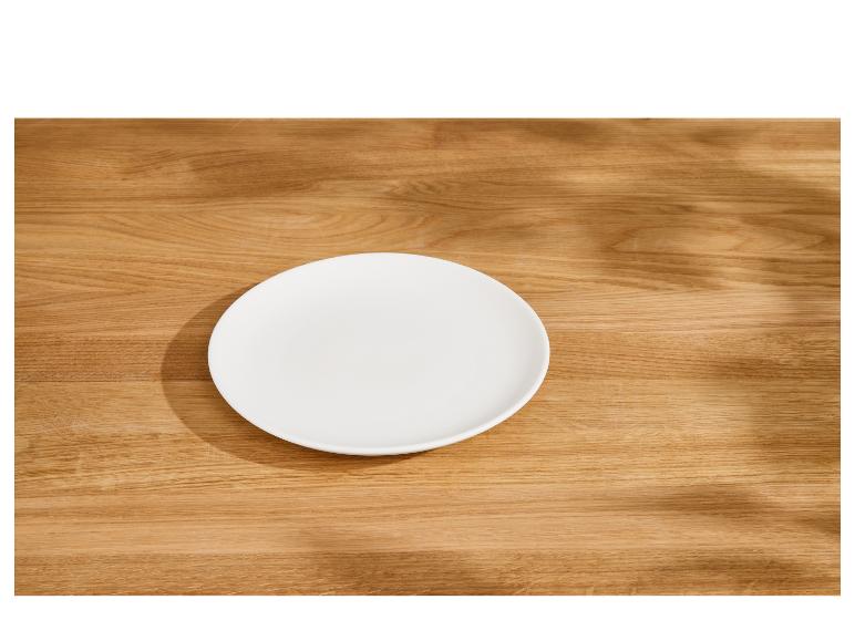 Leeg wit bord op een houten tafel met bladschaduwen