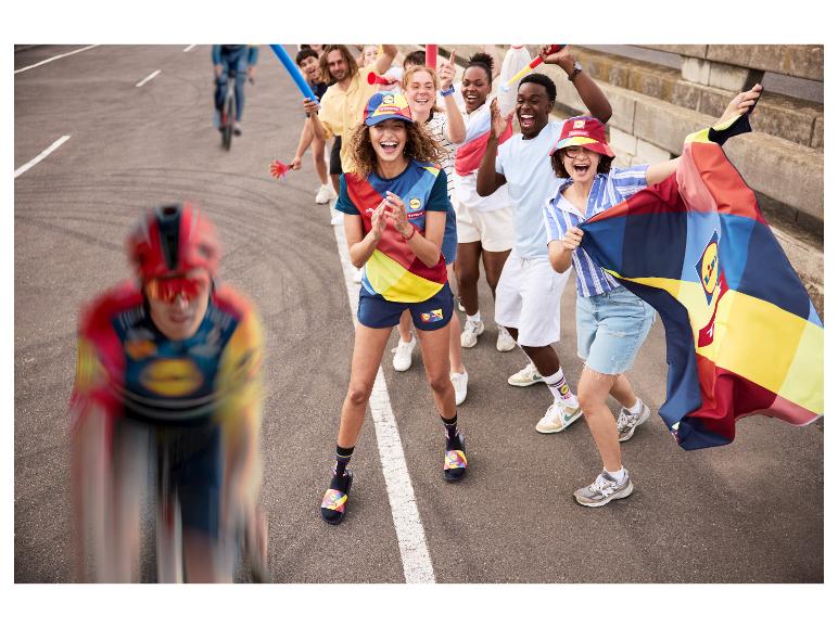 Fietsers en juichende fans in kleurrijke sportkleding, petten en sokken met een vlag.