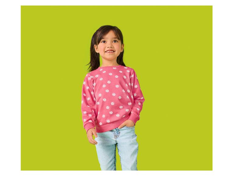 Lachend klein meisje in een roze bloemen trui en lichtblauwe jeans