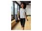 Vrouw in wit sportshirt en zwarte legging, met sporttas en waterfles.