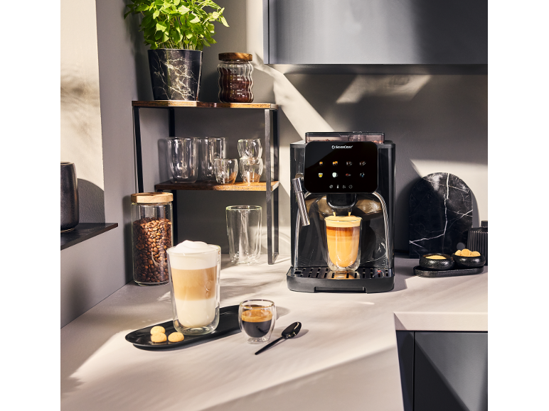 Koffiezetapparaat met twee kopjes koffie, koffiebonen en een plant in de keuken.