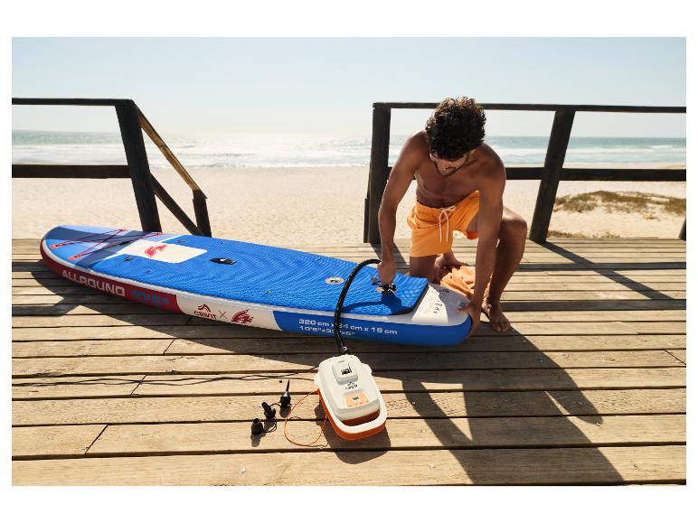 Man pompt CRIVIT SUP-board op het strand op met een elektrische pomp.
