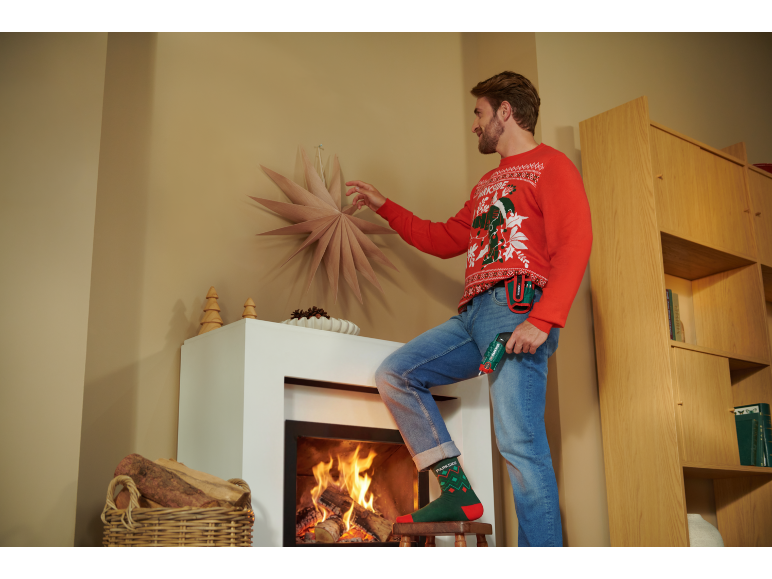 Man in kersttrui versiert de kamer met een accuschroevendraaier in zijn hand.