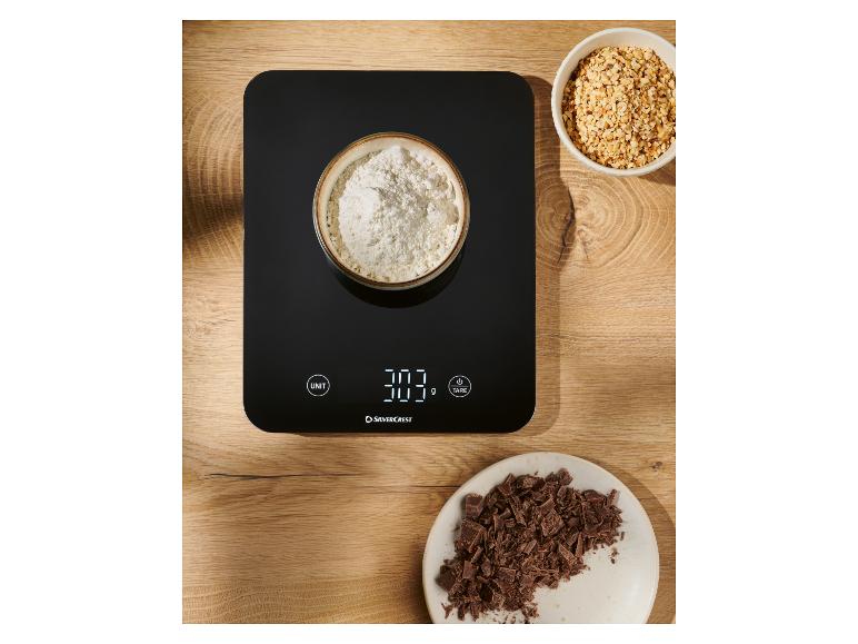 Zwarte digitale keukenweegschaal met een kom bloem, gehakte hazelnoten en chocolade.