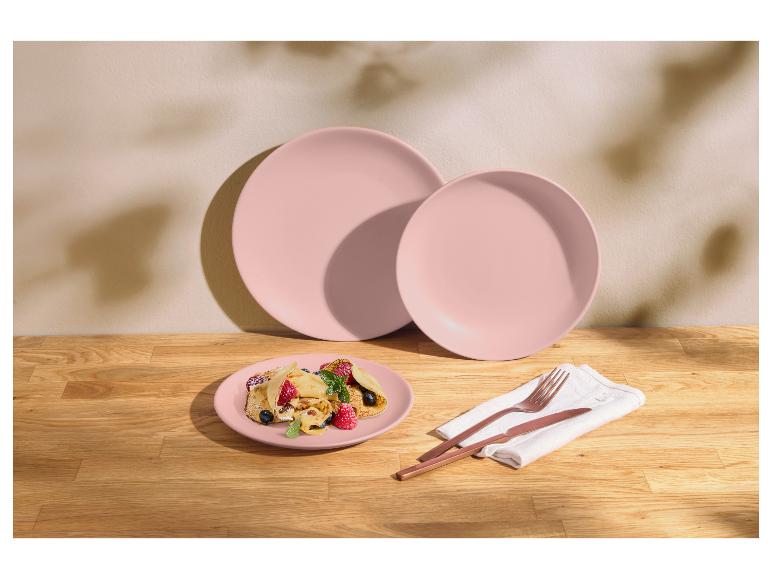 Pastelroze borden met fruitcrêpes en koperkleurig bestek op een houten tafel.