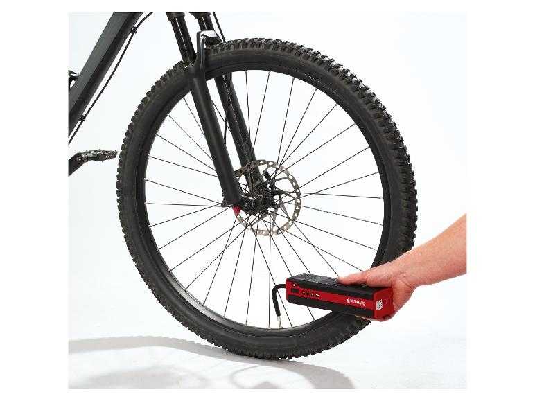 Een hand houdt een rode en zwarte draagbare luchtcompressor vast om een fietsband op te pompen.