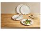 Witte borden met een vlees- en groentegerecht, bestek en een houten snijplank.