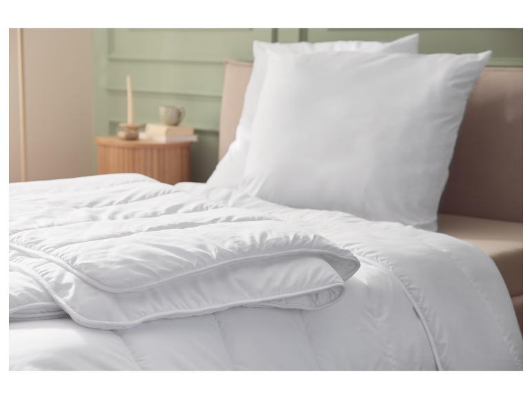 Wit dekbed en kussen op een bed, met slaapkamerinterieur op de achtergrond.
