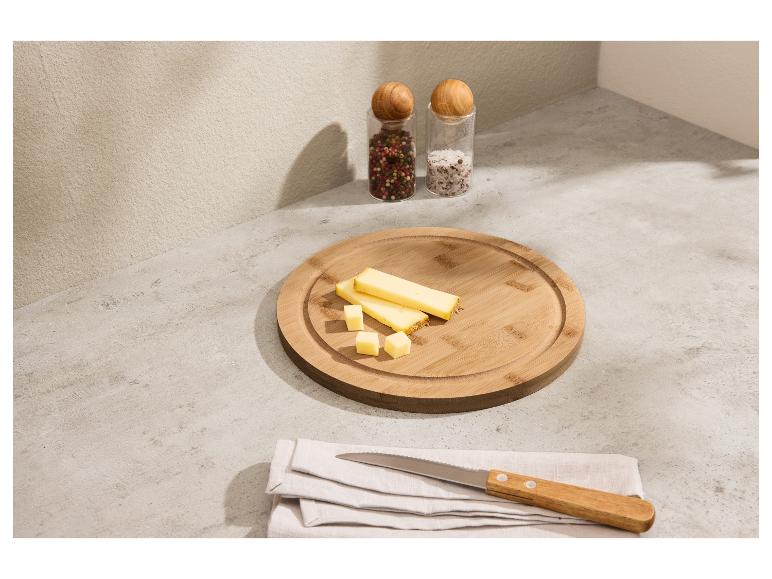 Gesneden kaas op een houten snijplank met kruidenmolens en een mes.