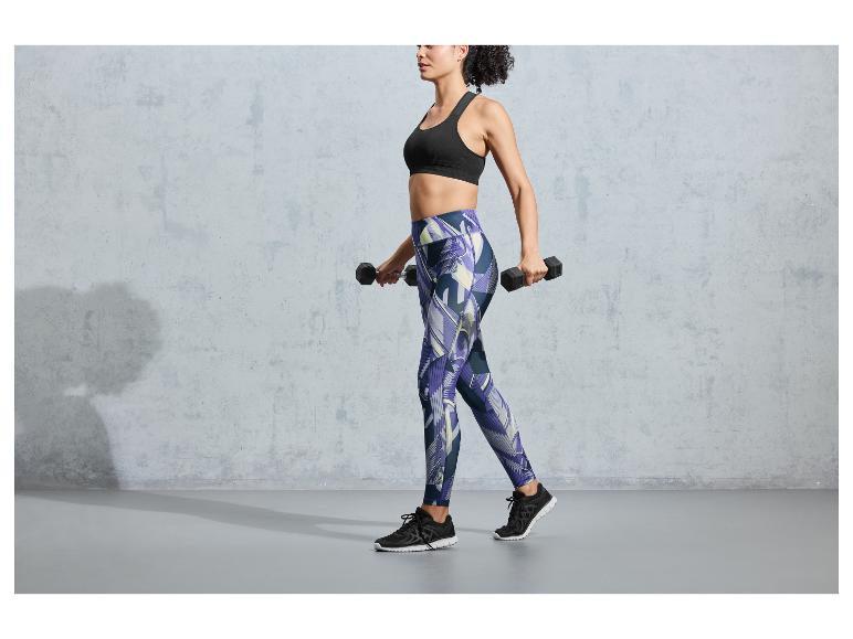 Een vrouw in een zwarte sportbeha en leggings met een printje tilt gewichten op.