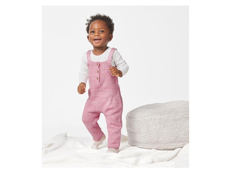 Een peuter in een roze gebreide romper speelt op een wit kleed.