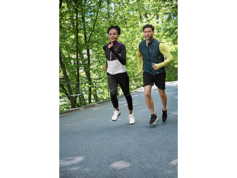 Twee hardlopers in sportkleding joggen buiten, vrouw in een jas en man in een vest.