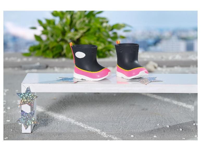 Zwarte en roze kinderregenlaarzen op een witte bank met sterdecoraties.